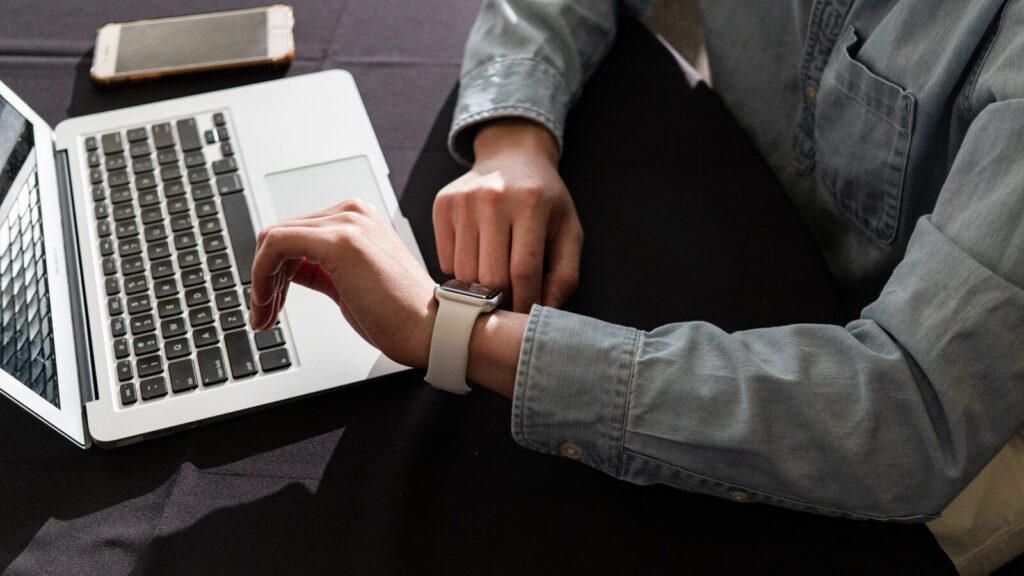 A karóráján időt ellenőrző felnőtt a laptopja mellett, a 10 perces hatékony angol tanulás otthoni alkalmazása közben.